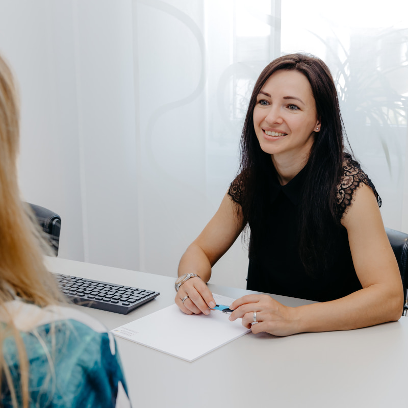 Eine Mitarbeiterin sitzt einer Mandantin gegenüber. Vor ihr liegt ein Block und sie hält einen Stift in der Hand.