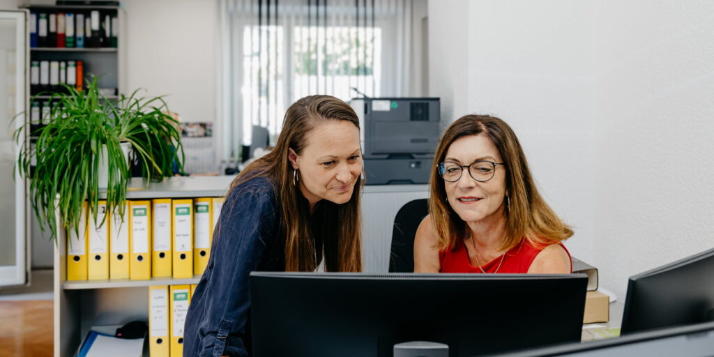 Zwei Mitarbeiterinnen der Steuerkanzlei Schicker & Kollegen besprechen am Monitor einen Vorgang