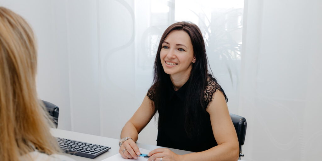 Eine Mitarbeiterin sitzt einer Mandantin gegenüber. Vor ihr liegt ein Block und sie hält einen Stift in der Hand.